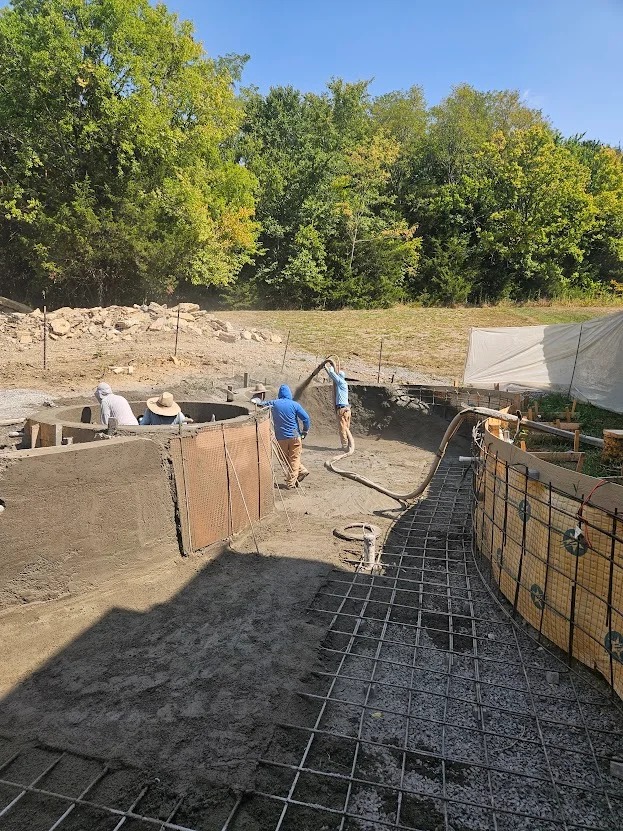 Crew placing concrete over rebar grid during gunite pool construction