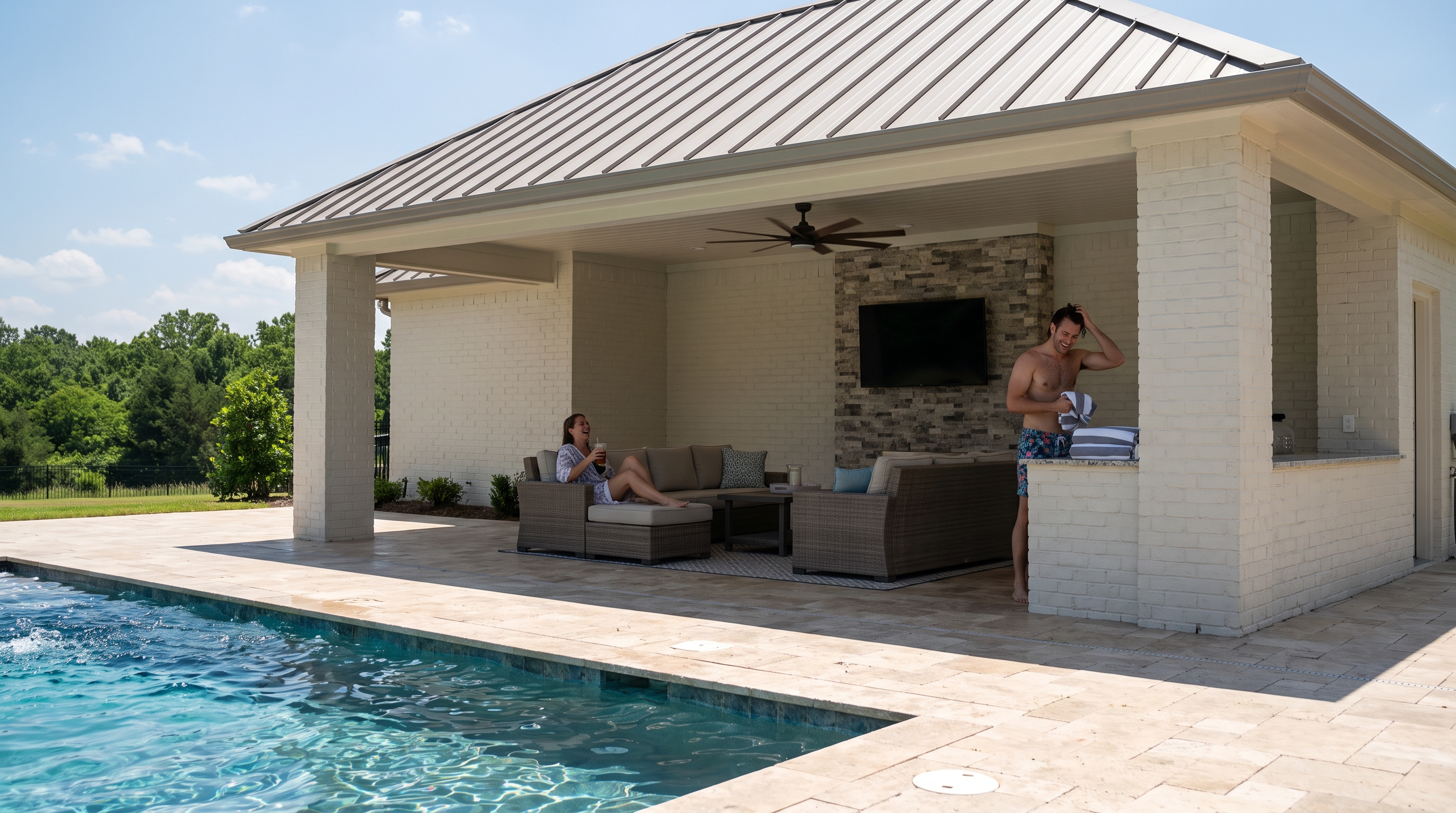Covered pool house with standing-seam roof, stone piers, sofas, and mounted TV beside a pool